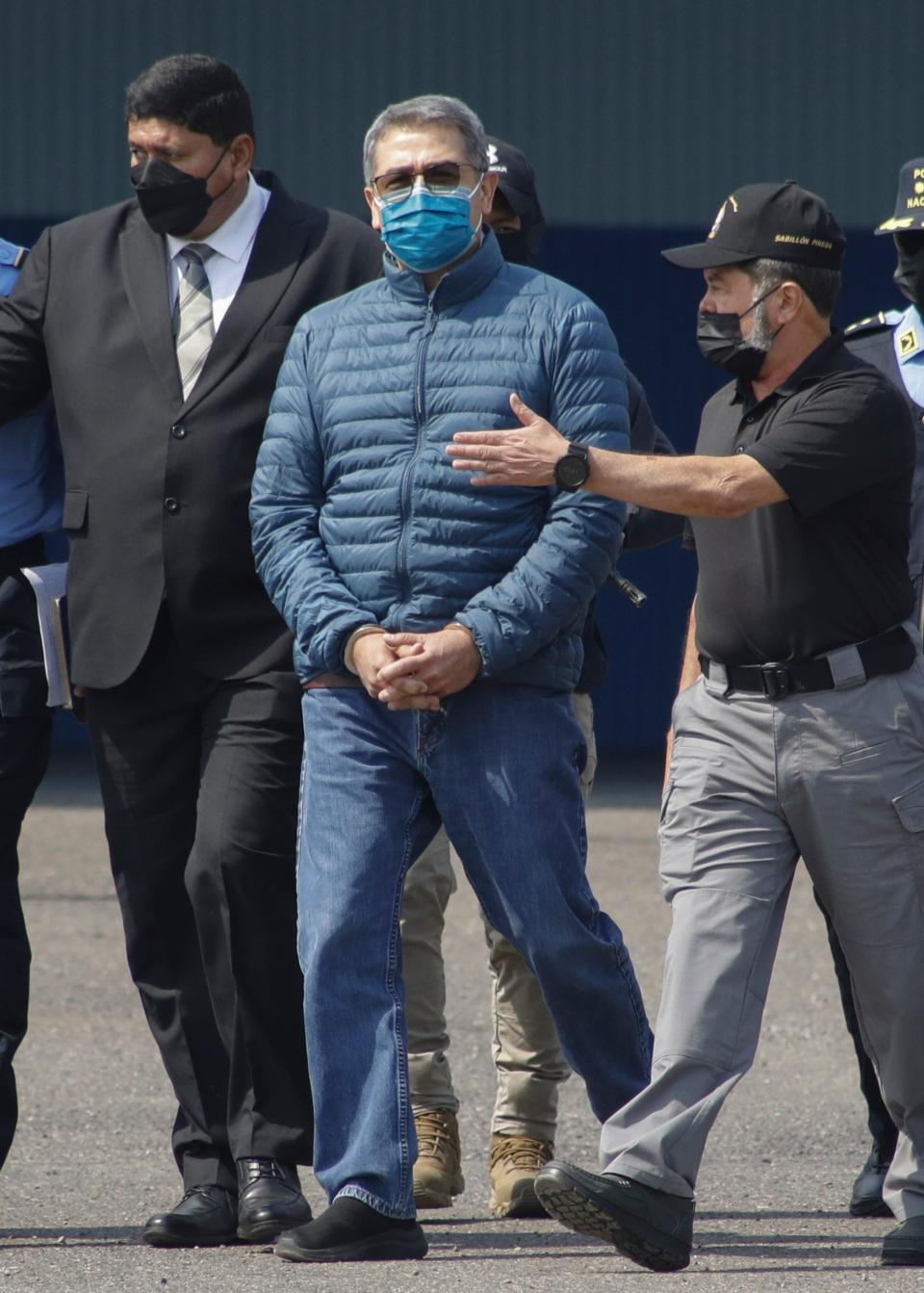 Former Honduran President Juan Orlando Hernandez, center, is taken in handcuffs to a waiting aircraft as he is extradited to the United States, at an Air Force base in Tegucigalpa, Honduras, Thursday, April 21, 2022. Honduras' Supreme Court approved the extradition of Hernandez to the United States to face drug trafficking and weapons charges.