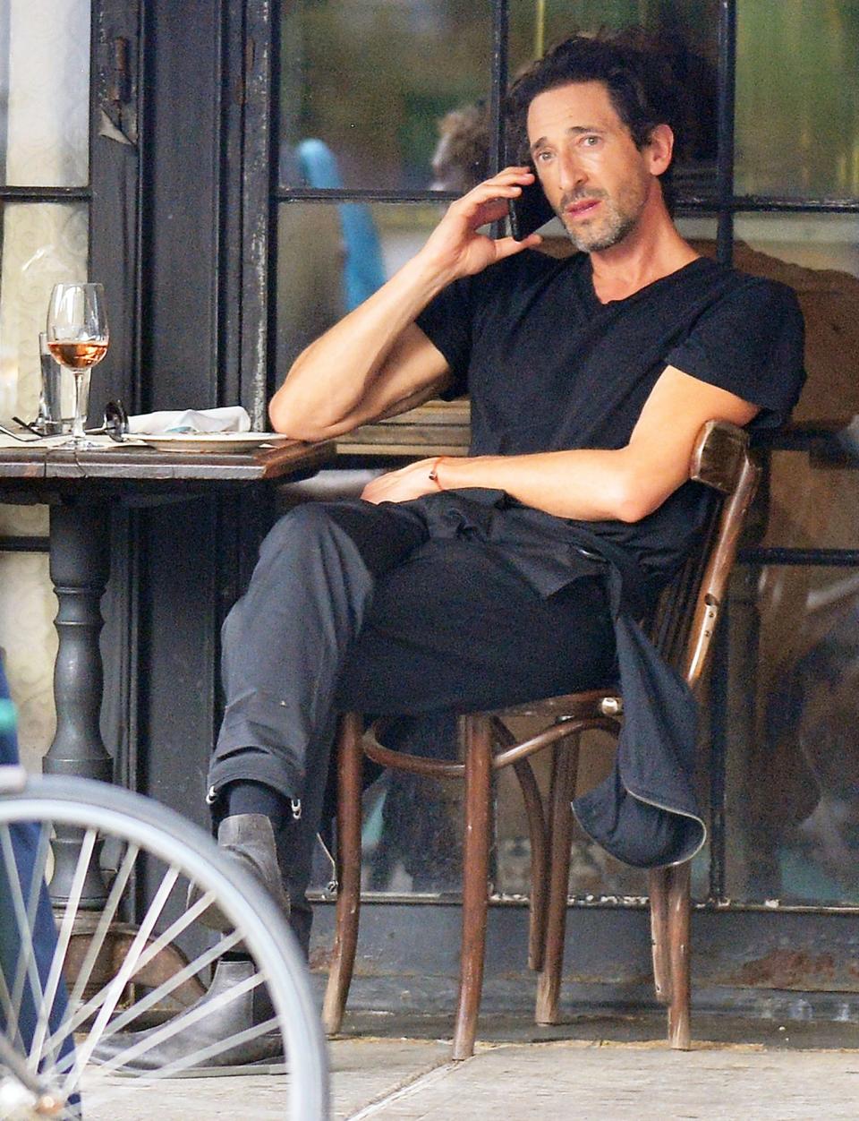 <p>An incognito Adrien Brody chats on his phone while enjoying a glass of wine outside at a New York City restaurant on Tuesday.</p>