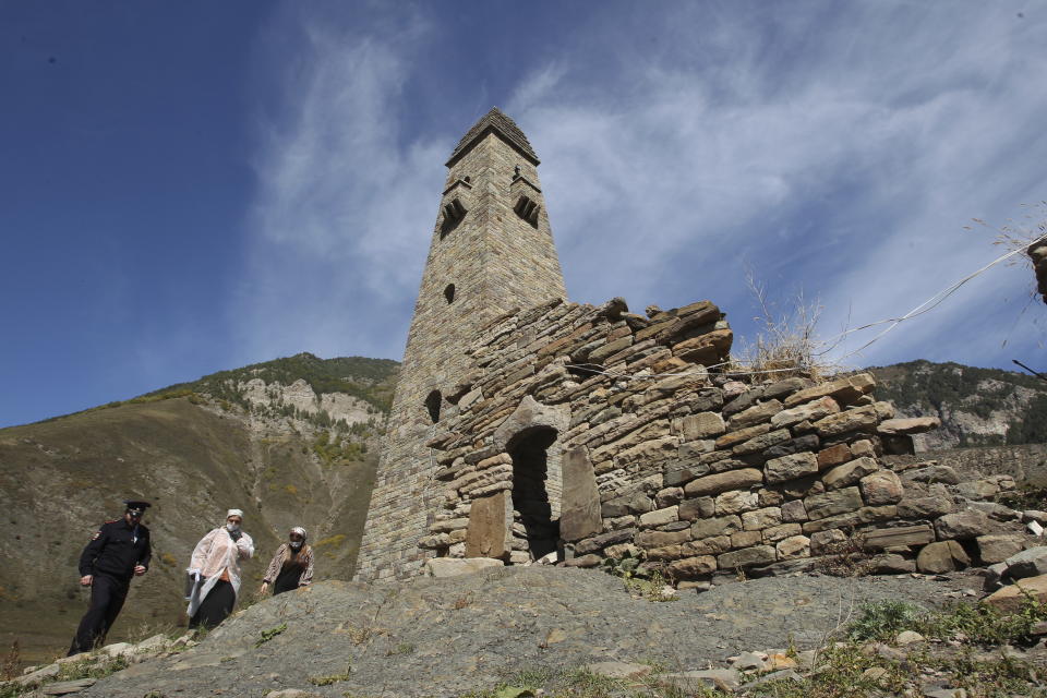 Members of a local election commission escorted by a police officer walk past an old defensive tower during the Parliamentary elections in Khimoy village, 115 kilometers (72 miles) southeast of Grozny, the capital of Chechen republic, southern Russia, Sunday, Sept. 19, 2021. Russia has begun the third day of voting for a new parliament that is unlikely to change the country's political complexion. There's no expectation that United Russia, the party devoted to President Vladimir Putin, will lose its dominance in the State Duma. (AP Photo/Musa Sadulayev)