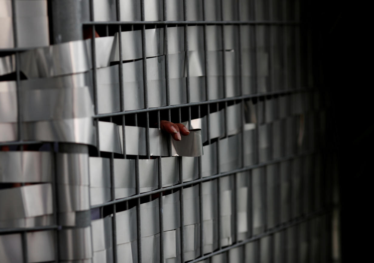 A worker's fingers peeking through a fence as he speaks with a friend to help with remittance at the S11 Dormitory@Punggol – gazetted to be an isolation area – on 6 April, 2020. (PHOTO: Reuters)