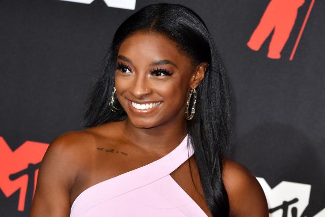 Simone Biles smiles in a pink, one-shoulder dress