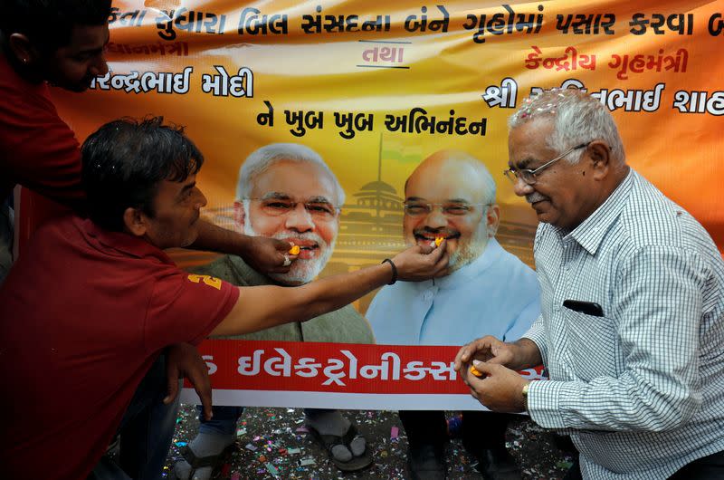 People, who claim to have migrated from Pakistan's Sindh Province, offer sweets to images of India's PM Modi and Home Minister Shah during celebrations after India's parliament passed a Citizenship Amendment Bill, in Ahmedabad