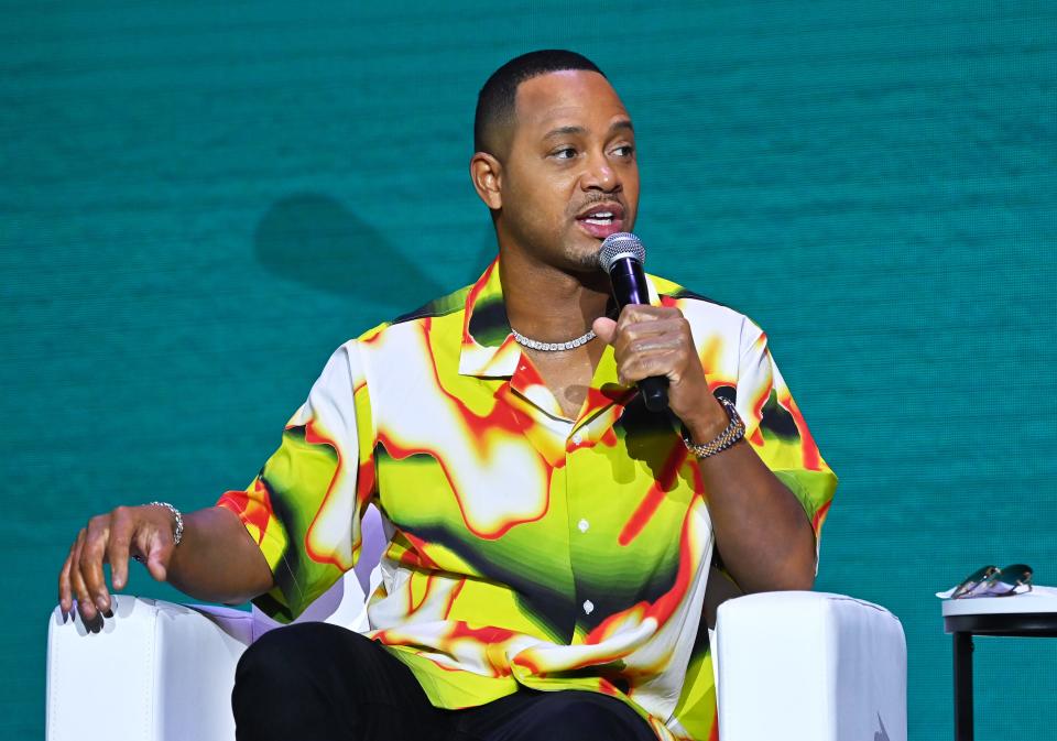 Terrence J sitting and speaking into a microphone in a green and and white shirt