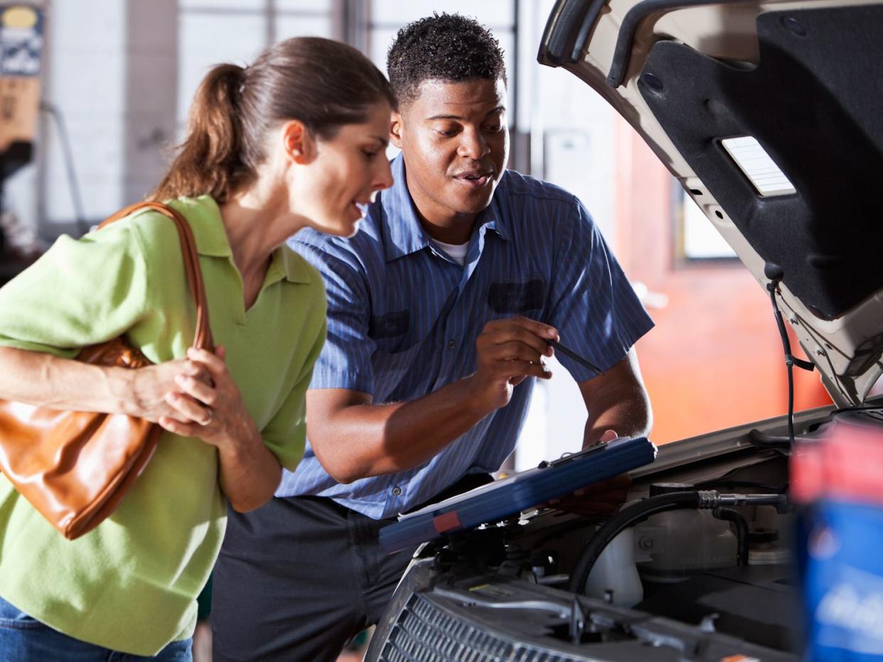 African American auto mechanic (30s) with female customer (40s) looking under car hood. Focus on man.