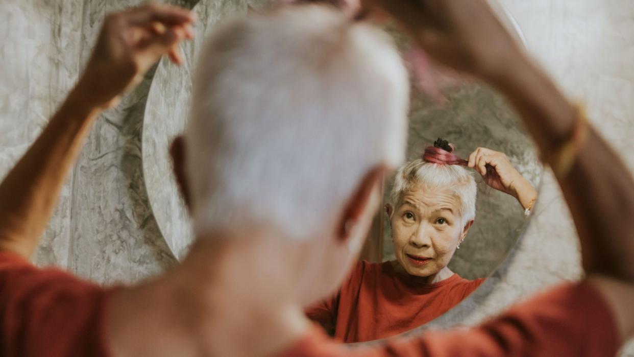 Older Asian woman doing her hair in the mirror