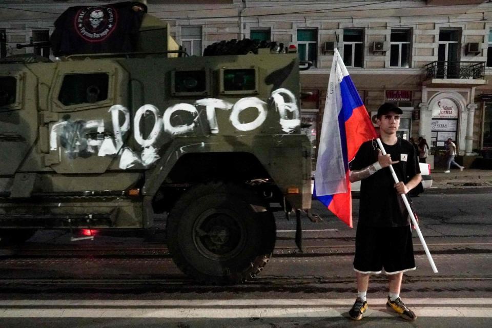 A man holds the Russian national flag in front of a Wagner group military vehicle with the sign read as 