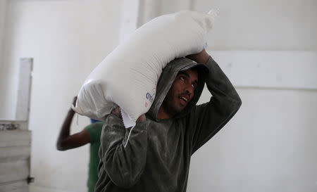 A Palestinian man carries a bag of flour at an aid distribution center run by United Nations Relief and Works Agency (UNRWA) in Khan Younis in the southern Gaza Strip September 1, 2018. REUTERS/Ibraheem Abu Mustafa