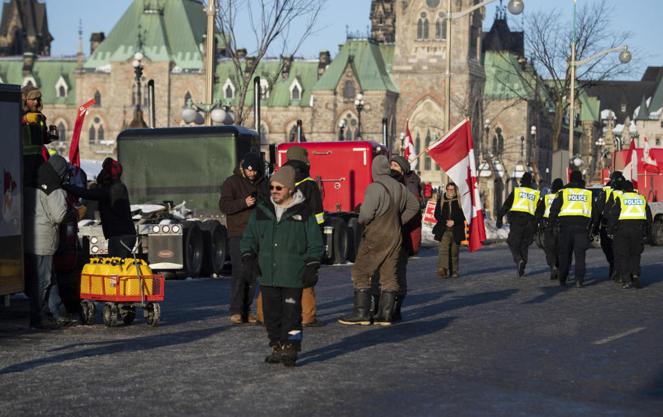 Ontario Provincial Police officers, right, walk past a group of people arranging fuel containers along Wellington Street in Ottawa on Monday, Feb. 7, 2022, as a protest against COVID-19 restrictions continues into its second week. A day earlier, Ottawa Police announced that anyone bringing material support to the protests, including gas, could be subject to arrest. (Justin Tang/The Canadian Press via AP)