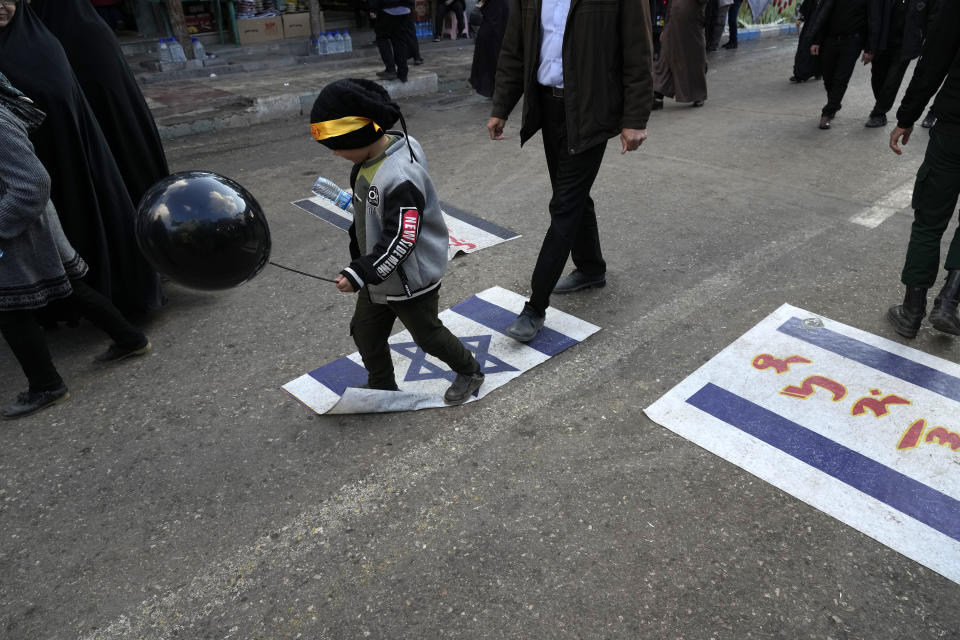 People walk on representations of the Israeli flag at the scene of Wednesday's bomb explosion in the city of Kerman about 510 miles (820 kms) southeast of the capital Tehran, Iran, Thursday, Jan. 4, 2024. Investigators believe suicide bombers likely carried out an attack on a commemoration for an Iranian general slain in a 2020 U.S. drone strike, state media reported Thursday, as Iran grappled with its worst mass-casualty attack in decades and as the wider Mideast remains on edge. (AP Photo/Vahid Salemi)