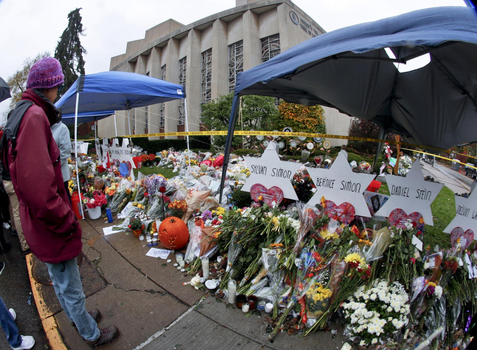 This photo made with a fisheye lens shows people standing beside hundreds of bouquets of flowers stacked in front of the memorials for victims of the deadly shooting a week ago at the Tree of Life Synagogue after an outdoor service on Saturday,Nov. 3, 2018, in Pittsburgh. Eleven people were killed and six others injured in a shooting during services last Saturday. (AP Photo/Keith Srakocic)