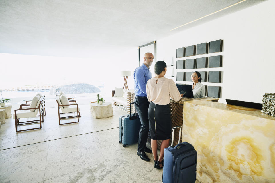 Two people with luggage check into a hotel at the reception, assisted by a receptionist