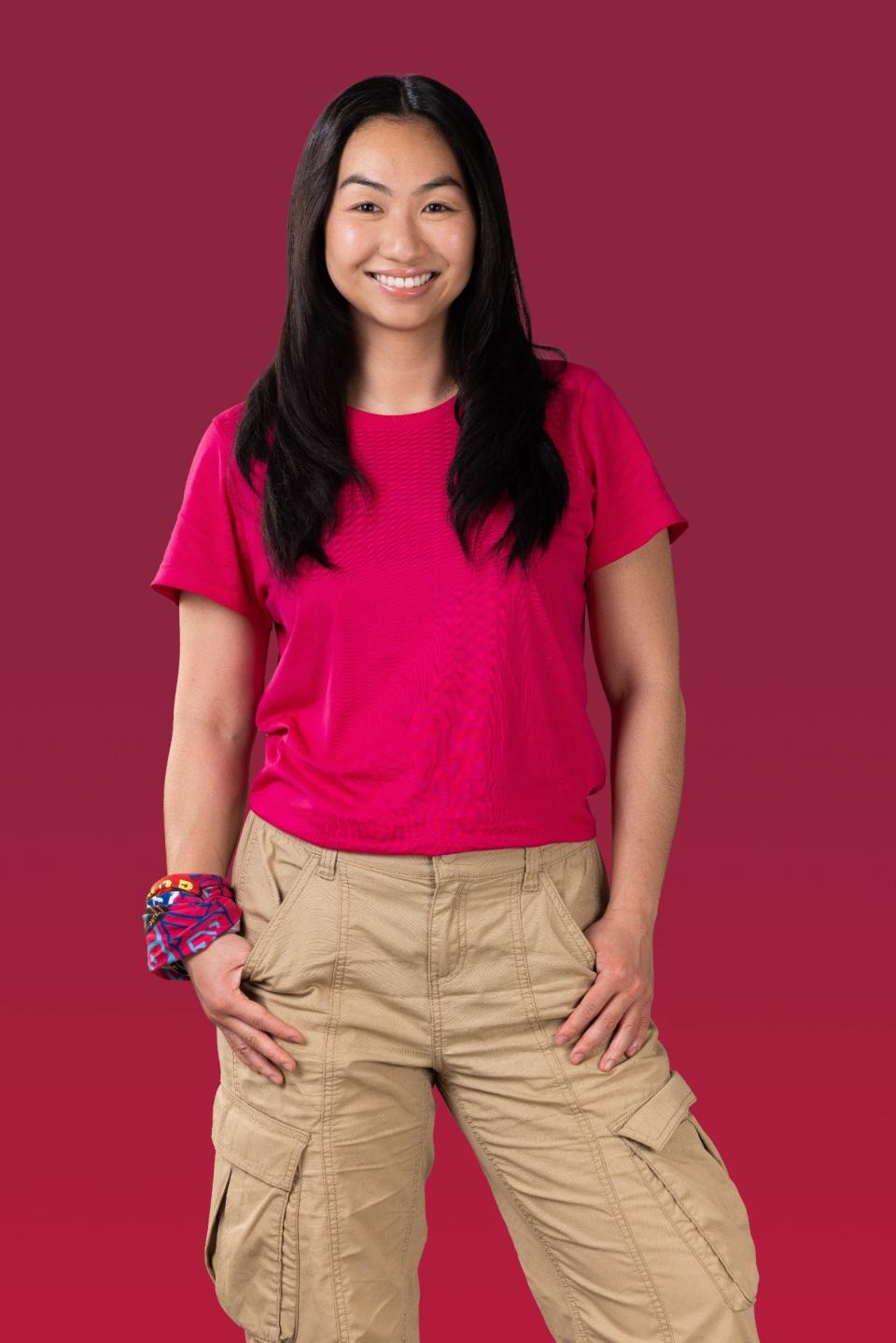 Aileen wears a pink t-shirt and smiles at the camera.