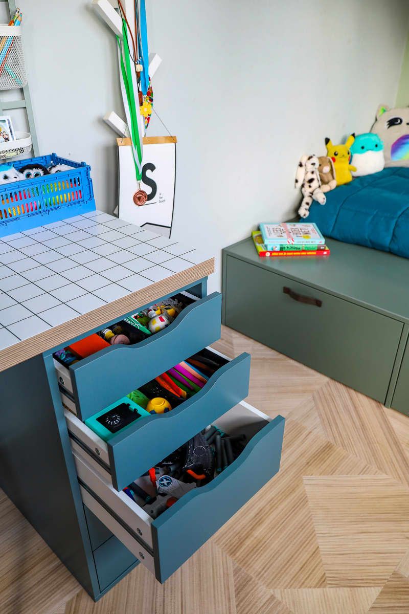 Cabinet under desktop holds child's items in neutral bedroom.