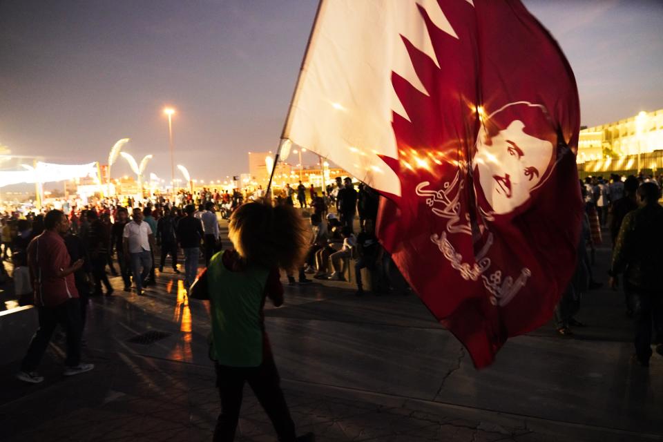 A woman waves a flag bearing the likeness of Qatar's ruling emir, Sheikh Tamim bin Hamad Al Thani, in Doha, Qatar, Friday, Nov. 18, 2022. Fans poured into Qatar on Friday ahead of the Middle East's first World Cup as Doha ordered beers not to be poured out at stadiums during the tournament — a last-minute surprise largely welcomed by the country's conservative Muslims and shrugged off by giddy fans. (AP Photo/Jon Gambrell)