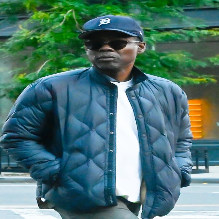 Chris walks outside while wearing a light jacket and a baseball cap