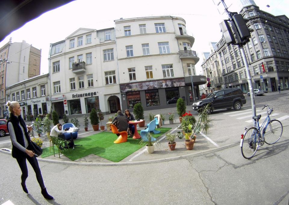 A woman walks past people participating in a PARK(ing) Day event in Riga