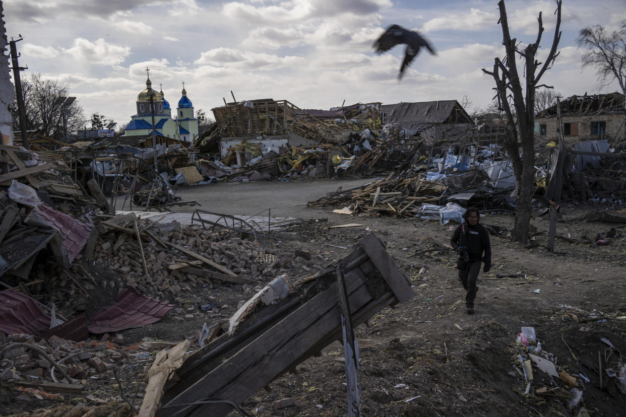 A journalist walks amid the destruction after a Russian attack in Byshiv, in the outskirts of Kyiv, Ukraine, Sunday, March 27, 2022. Ukrainian President Volodymyr Zelenskyy accused the West of lacking courage as his country fights to stave off Russia's invading troops, making an exasperated plea for fighter jets and tanks to sustain a defense in a conflict that has ground into a war of attrition. (AP Photo/Rodrigo Abd)