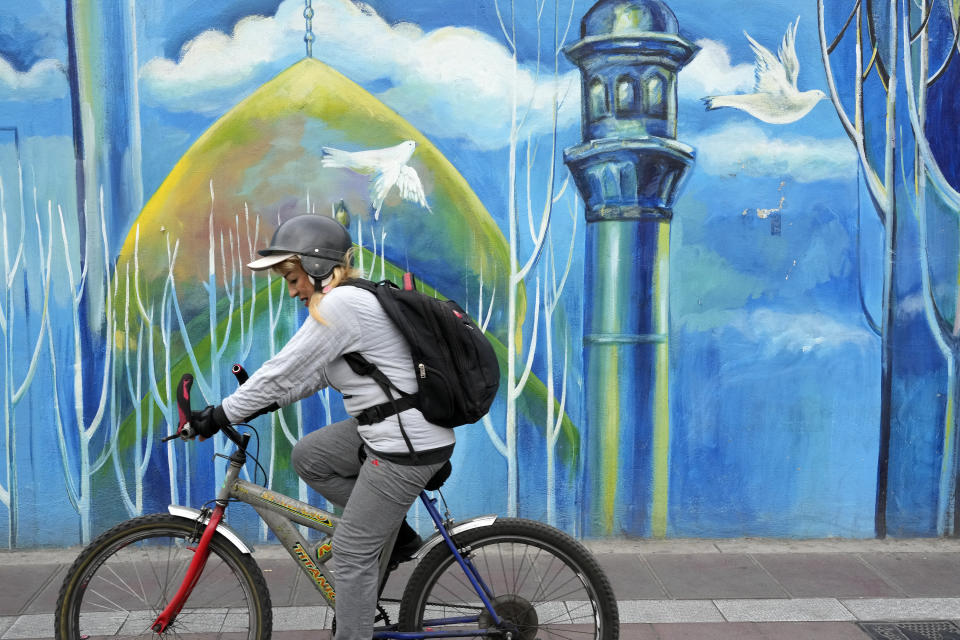 A woman rides her bicycle in front of mural of a mosque, in downtown Tehran, Iran, Thursday, Feb. 22, 2024. Candidates for Iran's March 1, parliamentary election began campaigning Thursday in the country's first election since the bloody crackdown on the 2022 nationwide protests that followed the death of 22-year-old Mahsa Amini in police custody. (AP Photo/Vahid Salemi)