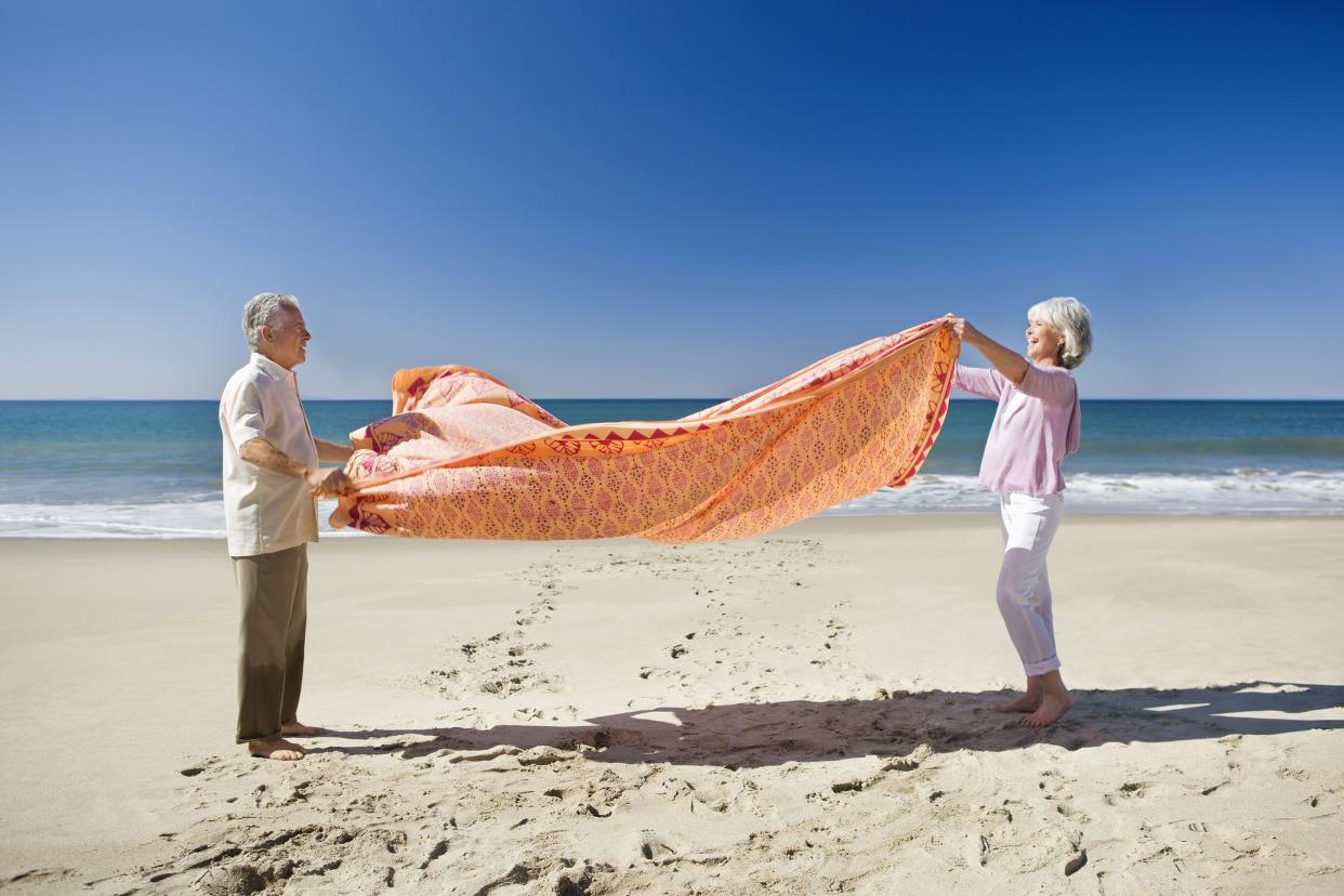 Senior couple spreading blanket on beach