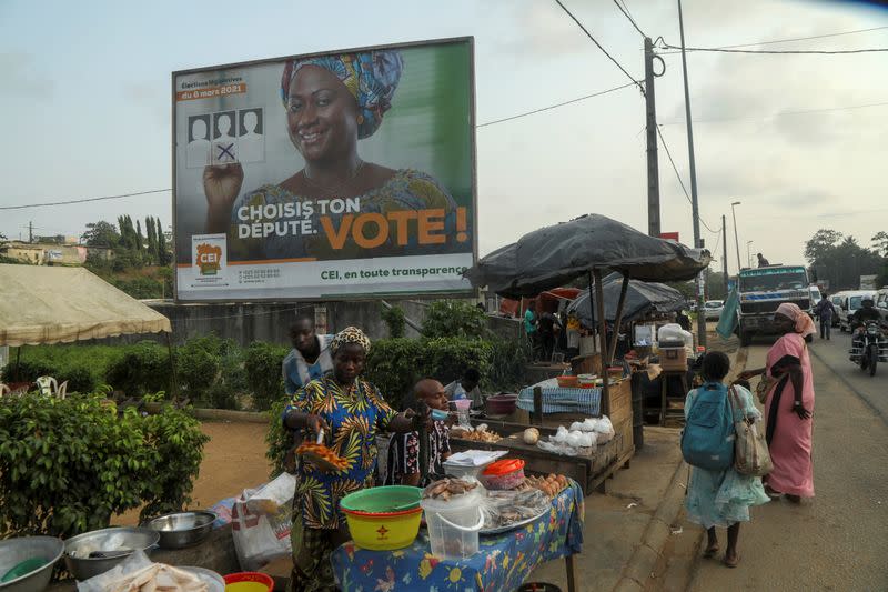 People move next to an awarness campaign billboard ahead of the legislative election in Abidjan