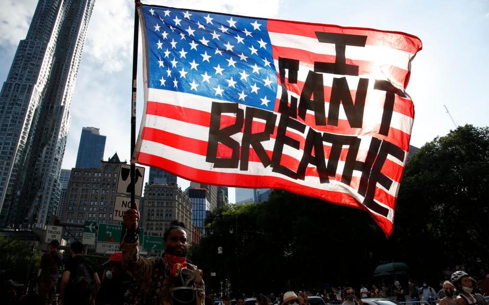 A protester holds an American flag with the words "I Can't Breathe" as he walks in Manhattan after a George Floyd Memorial demonstration in Brooklyn in June - JASON SZENES/EPA-EFE/Shutterstock