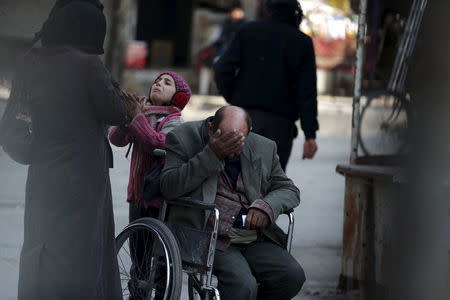 A girl with her father in a wheelchair, asks for help to pay a medical bill from passers by, in Douma, Syria February 3, 2016. REUTERS/Bassam Khabieh