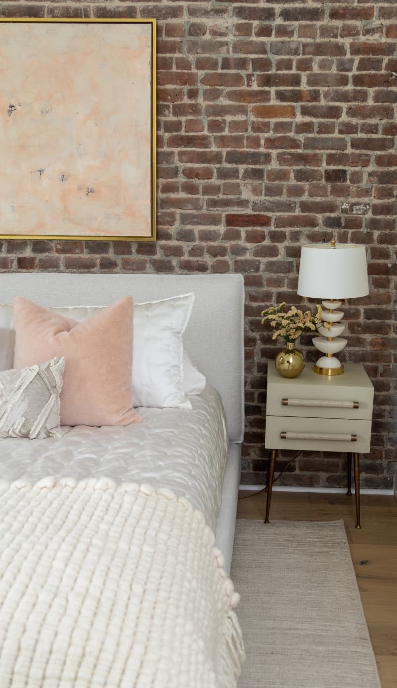 Brick-walled bedroom with white comforter, and white and pink decorative pillows.