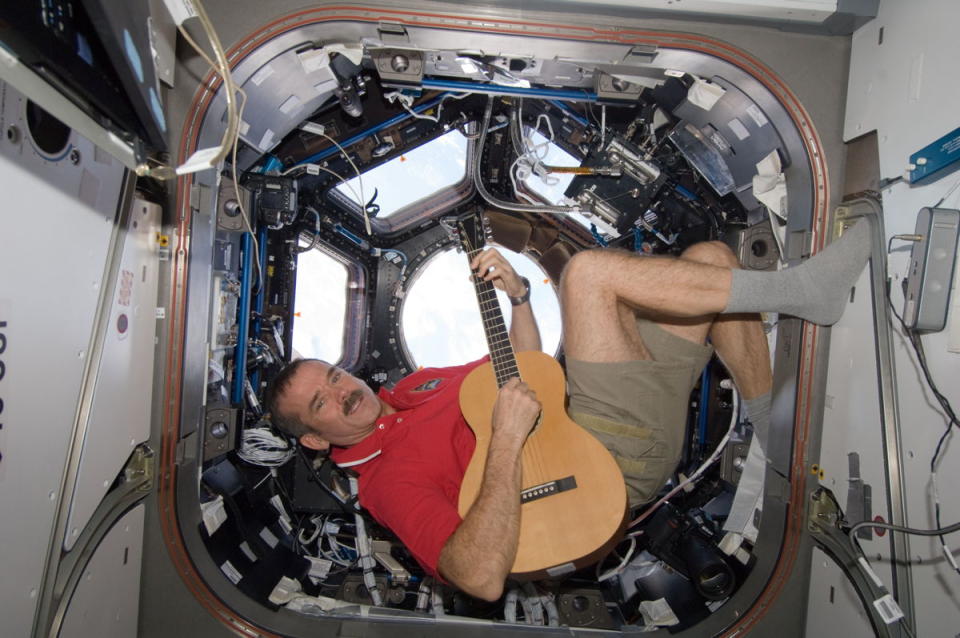 a man plays a guitar in a cramped room full of wires and screens while floating sideways