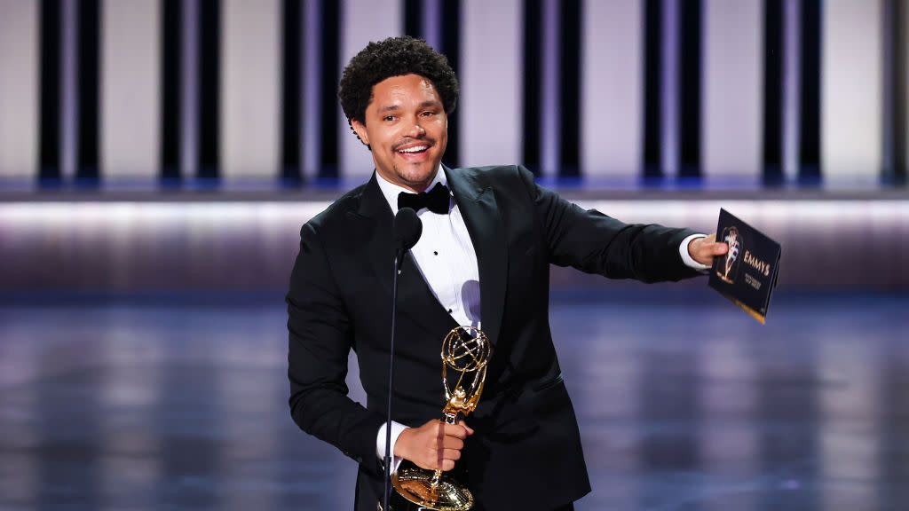 trevor noah holding his emmy award as he points out toward the crowd during his acceptance speech he is wearing a black tuxedo and bowtie