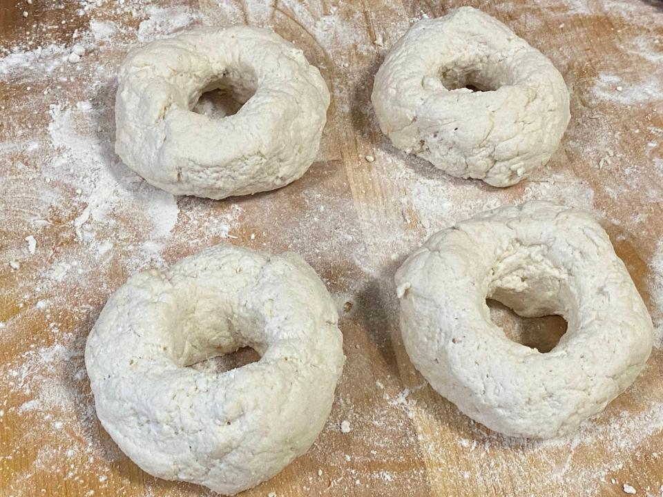 four bagel-shape pieces of dough on a floured surface