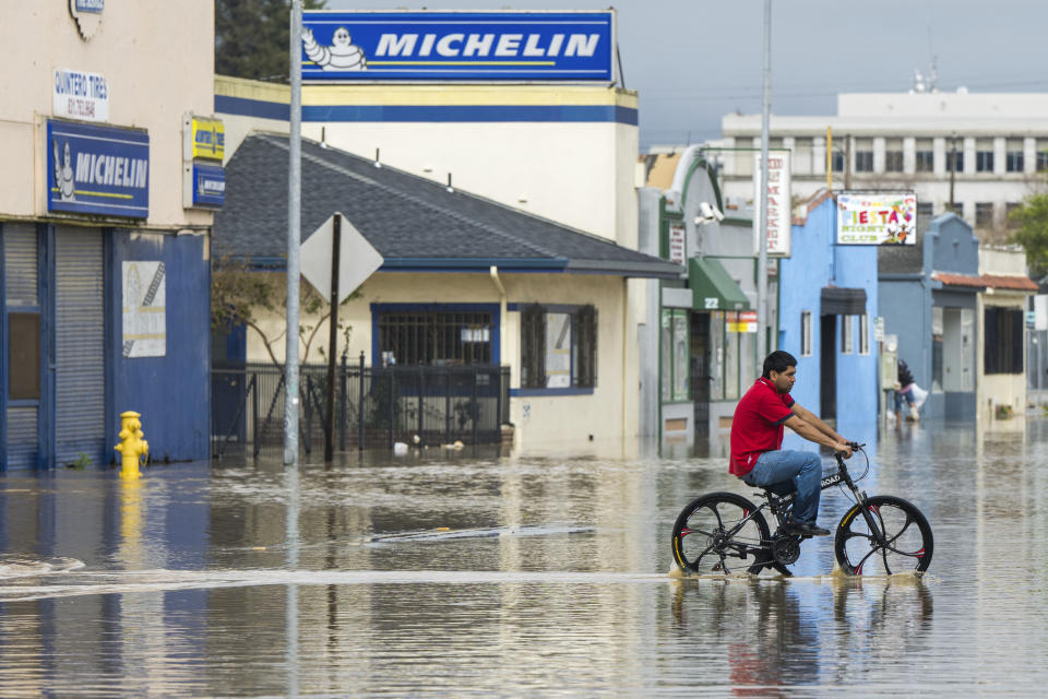 A man rides his bicycle through floodwaters in Watsonville, Calif., Saturday, March 11, 2023. Gov. Gavin Newsom has declared emergencies in 34 counties in recent weeks, and the Biden administration approved a presidential disaster declaration for some on Friday morning, a move that will bring more federal assistance. (AP Photo/Nic Coury)