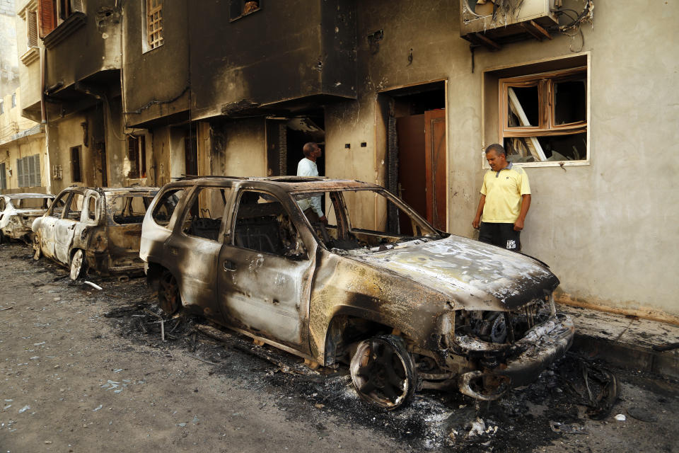 Men survey the remains of cars burned during clashes on a street in the Libyan capital of Tripoli, Sunday, August 28 2022. Deadly clashes broke out Saturday in Libya's capital between militias backed by its two rival administrations, portending a return to violence amid a long political stalemate. (AP Photo/Yousef Murad)