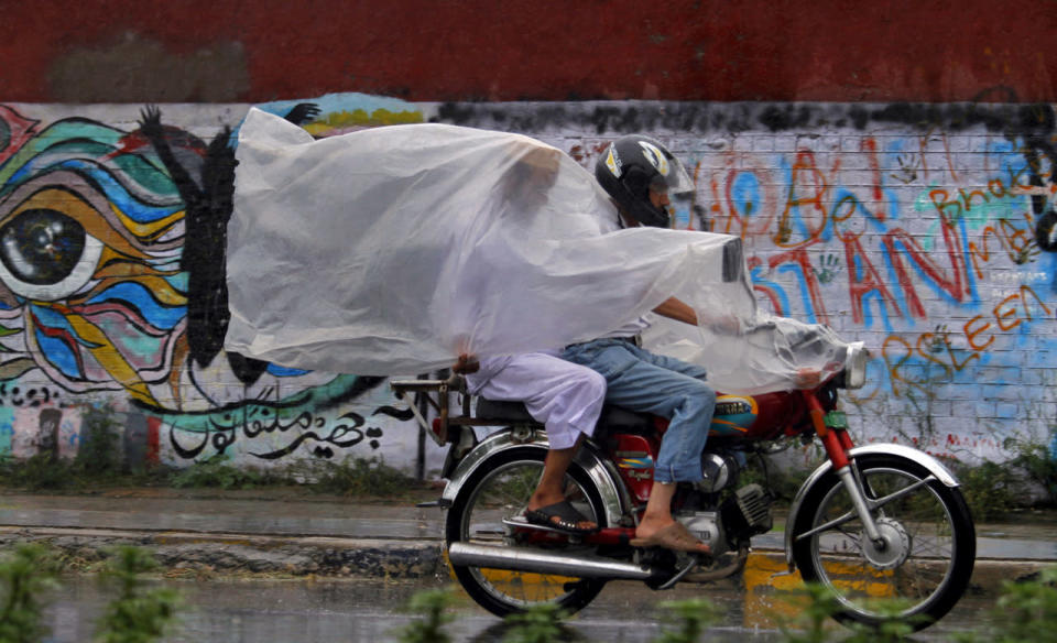 <p>Pakistanis use a plastic sheet to protect themselves from rain in Rawalpindi, Pakistan, July 27, 2016. Monsoon season in Pakistan begins in July and ends in September. (Photo: Anjum Naveed/AP)</p>