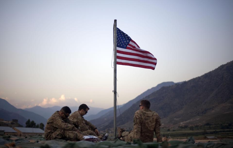 FILE - In this Sept. 11, 2011 file photo, US soldiers sit beneath an American flag just raised to commemorate the tenth anniversary of the 9/11 attacks at Forward Operating Base Bostick in Kunar province, Afghanistan. The Biden administration’s surprise announcement in April 2021, of an unconditional troop withdrawal from Afghanistan by Sept. 11, 2021, appears to strip the Taliban and the Afghan government of considerable leverage, pressuring them to reach a peace deal. (AP Photo/David Goldman, File)