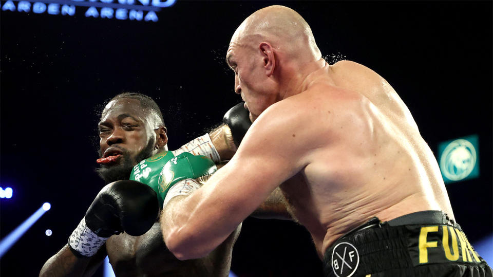 Tyson Fury (R) punches Deontay Wilder in the face.