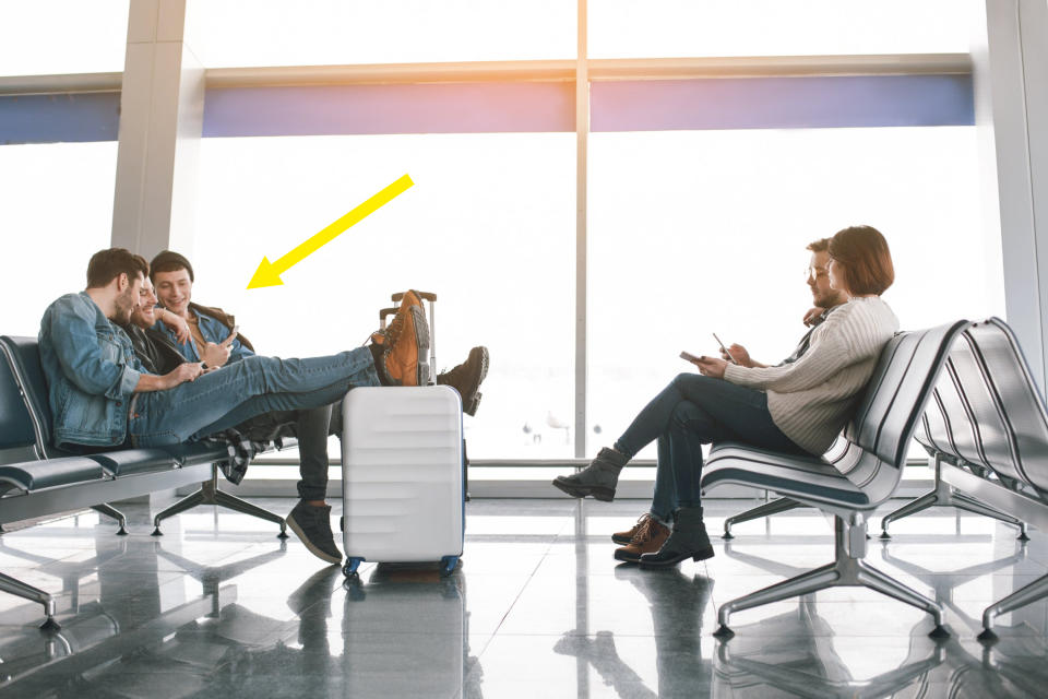 Four people sitting in an airport terminal waiting area. Two men on the left are having a conversation, while a man and a woman on the right are using their phones
