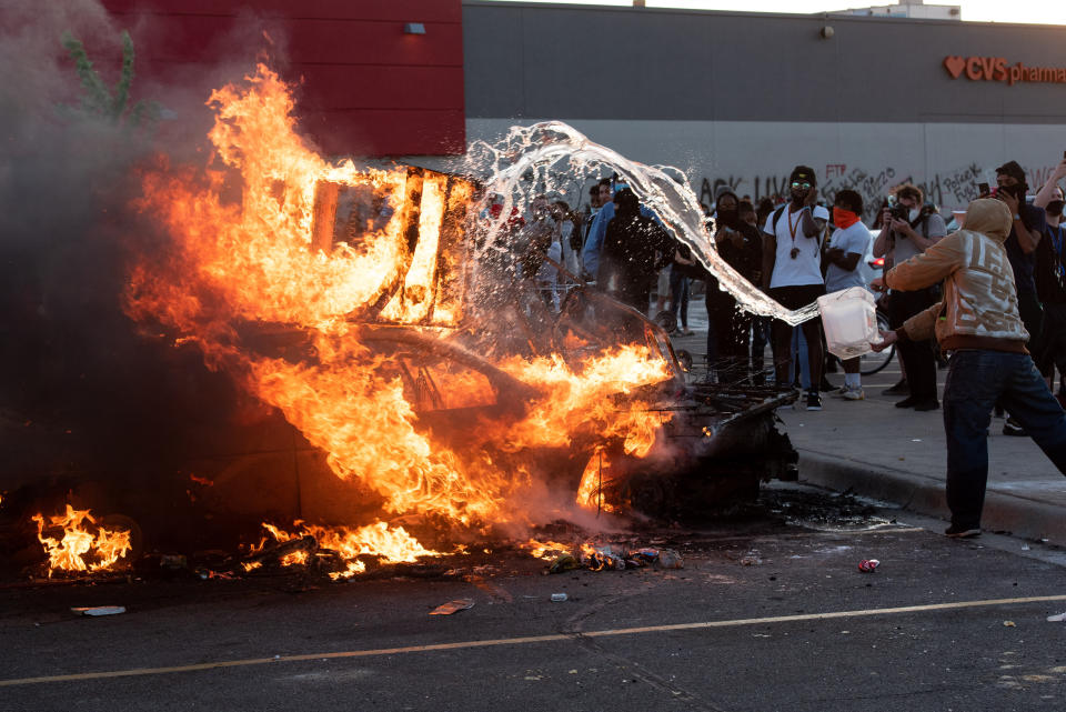 Un joven intenta avivar las llamas de un coche que ha sido incendiado por los manifestantes este 28 de mayo. (Foto: Steel Brooks / Anadolu Agency / Getty Images).