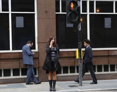 A woman waits to cross the street, as a man looks at his mobile phone and another walks past in the City of London, June 13, 2013. REUTERS/Olivia Harris