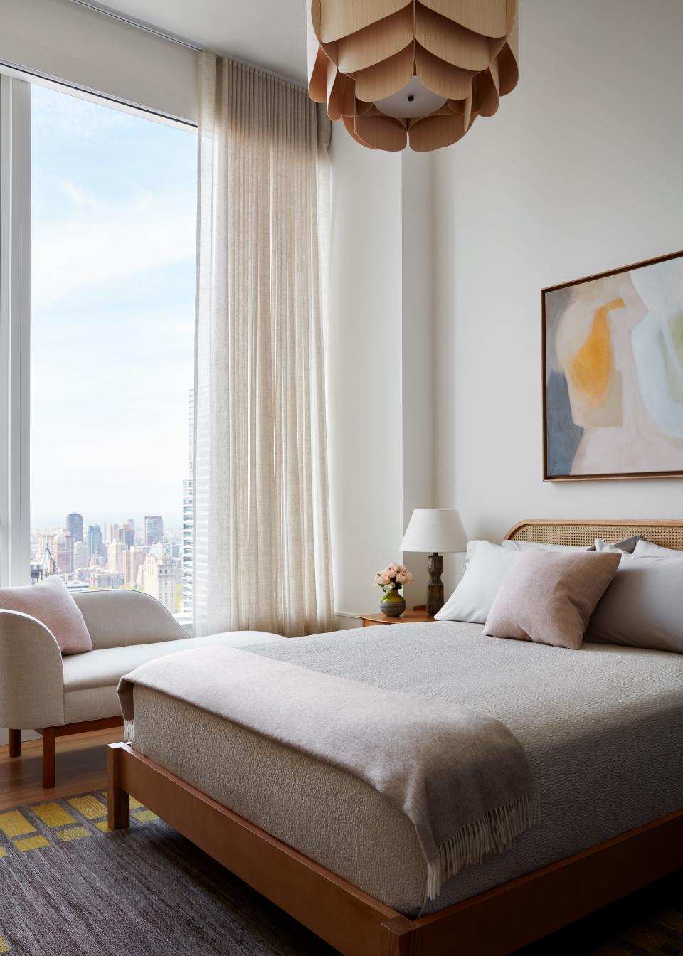 Warm wood tones and pink and beige textiles add feminine flair to the guest bedroom. Scott designed a custom chaise with wood cylinder legs from Anthony Lawrence and fabric by Merry Mullings. Pops of yellow appear in the vintage Swedish kilim rug and Amy Kirchner painting above the caned headboard. The ceiling fixture is from Trans-Luxe.