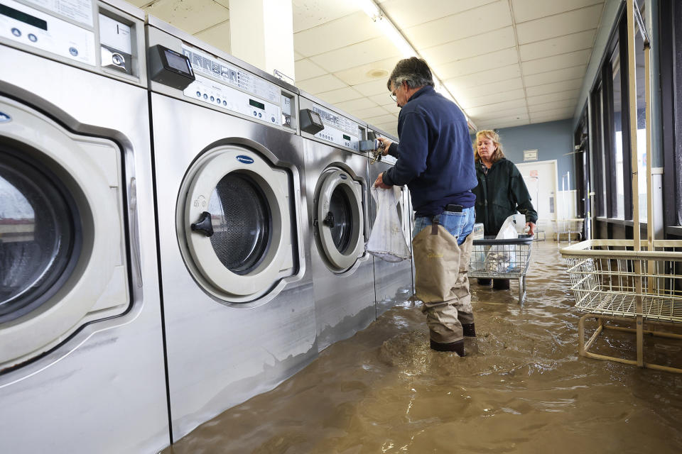Patrick Cerruti, left, and his wife, Pamela Cerruti take coins out of washing machines inside the flooded Pajaro Coin Laundry in Pajaro, California, on March 14, 2023.