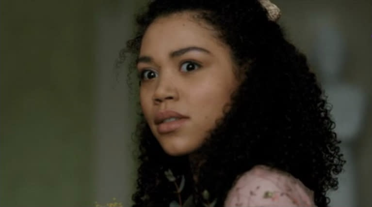 A young woman on screen with curly hair and a floral patterned top, looking off to the side