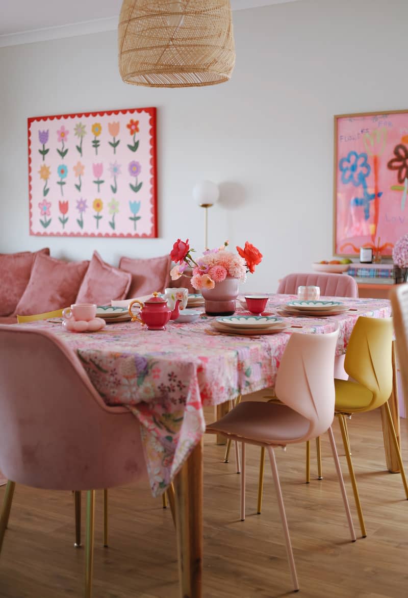 white dining room with pale pink and yellow chairs at dining table with floral tablecloth