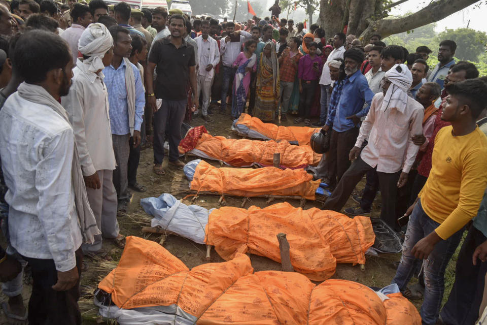 Villagers gather around the bodies of victims of a road accident in Kanpur, Uttar Pradesh state, India, Sunday, Oct.2, 2022. A farm tractor pulling a wagon loaded with people overturned and fell into a pond in Kanpur city's Ghatampur area Saturday night killing 26 people, most of them women and children. (AP Photo)