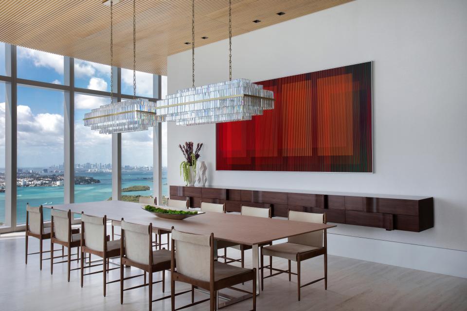 In this Miami penthouse by Jaegger Interior Design, the dining room boasts a sleek light oak and brass table complemented by ten Sergio Rodrigues chairs. Adjacent, a piece by the late kinetic master Carlos Cruz-Diez adds an extra layer of artistic allure.