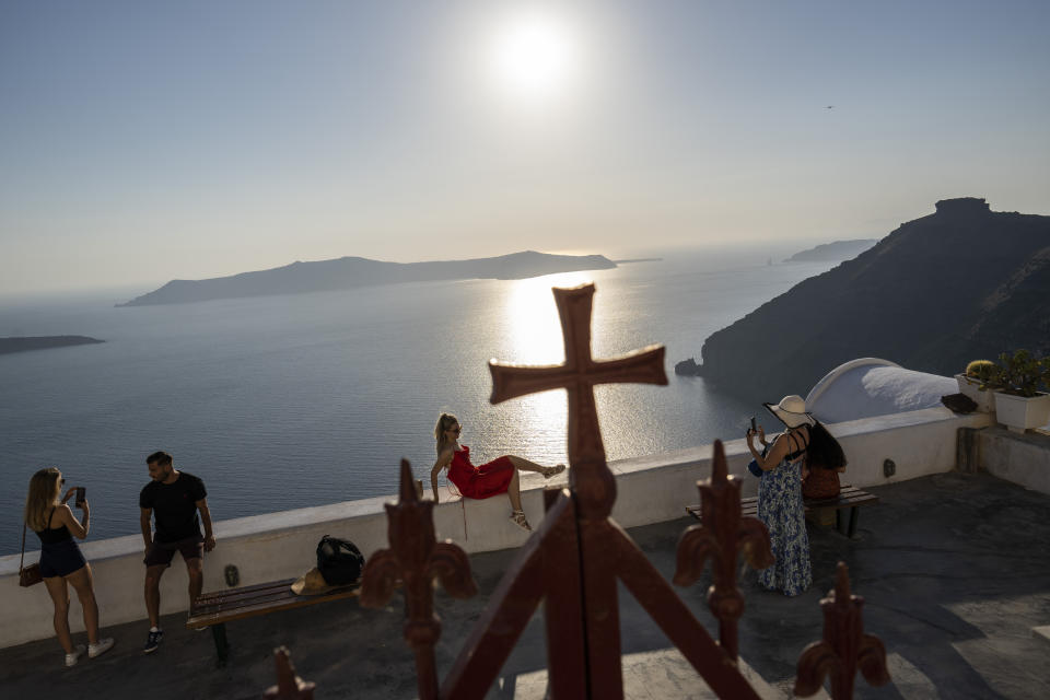 Una mujer posa para una fotografía frente a la Iglesia Católica de la Dormición de la Virgen María en la isla griega de Santorini el 15 de junio de 2022. (Foto AP/Petros Giannakouris).