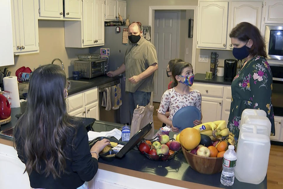 Michael, center, and Jeanine Waterman, right, prepare a family meal at their home in Hanover, Mass., a suburb of Boston, on Wednesday, Oct. 28, 2020. After the St. Francis of Assisi School in Braintree announced its closure in June as the school year ended, Michael and Jeanine’s three children are learning at home. “What angers us,” Michael said, “is that we feel like, given the amount of money that the Catholic Church has, they absolutely could have remained open.” (AP Photo/Rodrique Ngowi)