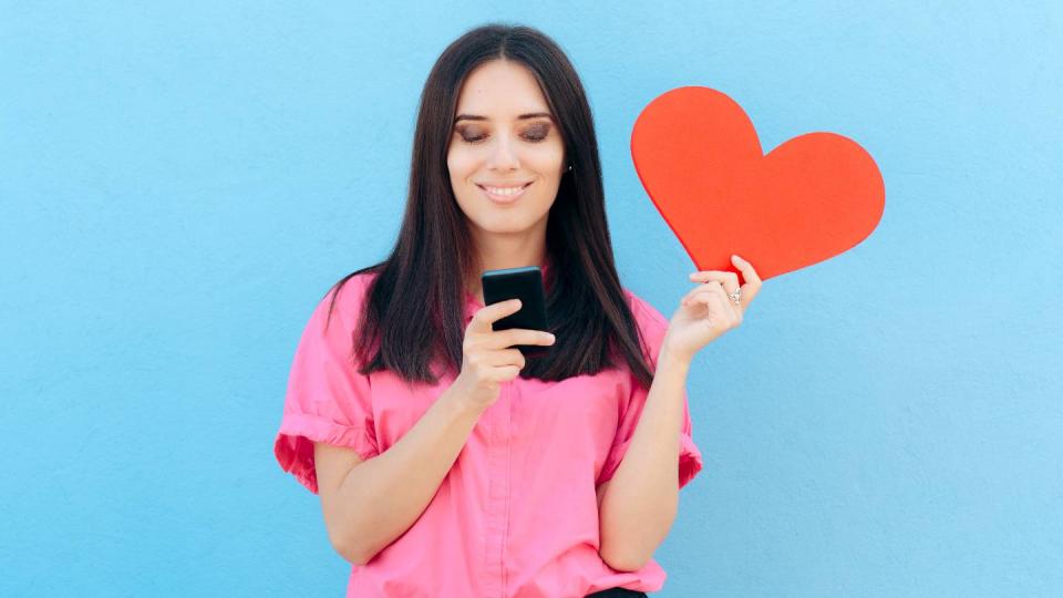 Une femme consulte un smarphone, un coeur dans la main