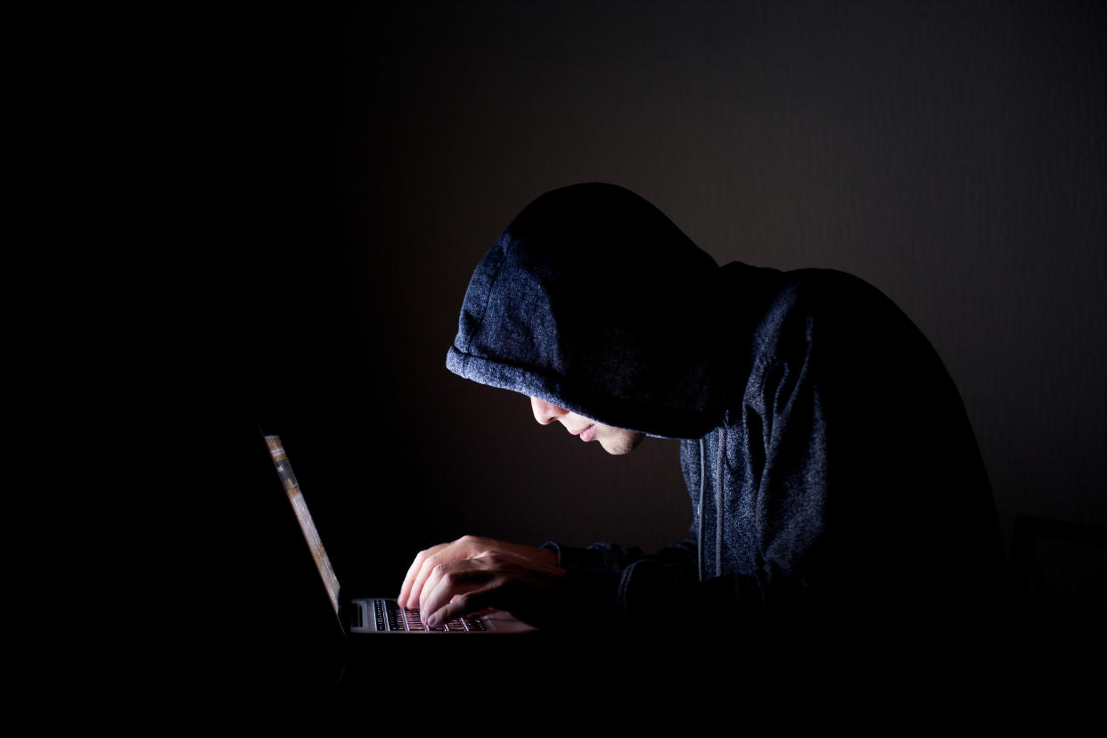 A hooded man looking at his laptop in the dark