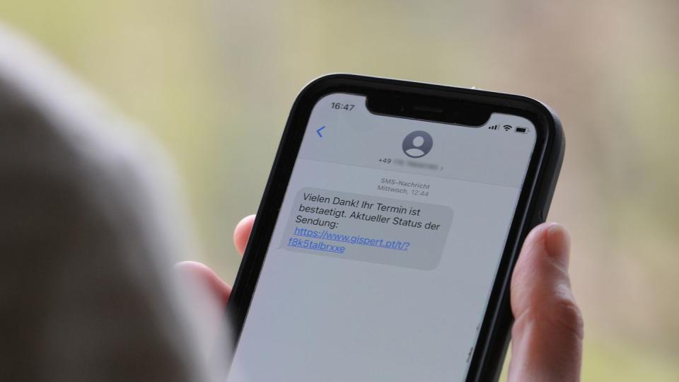 Eine Frau hält ein Smartphone in ihrer Hand, auf dessen Display eine Betrugs-SMS zu lesen ist.