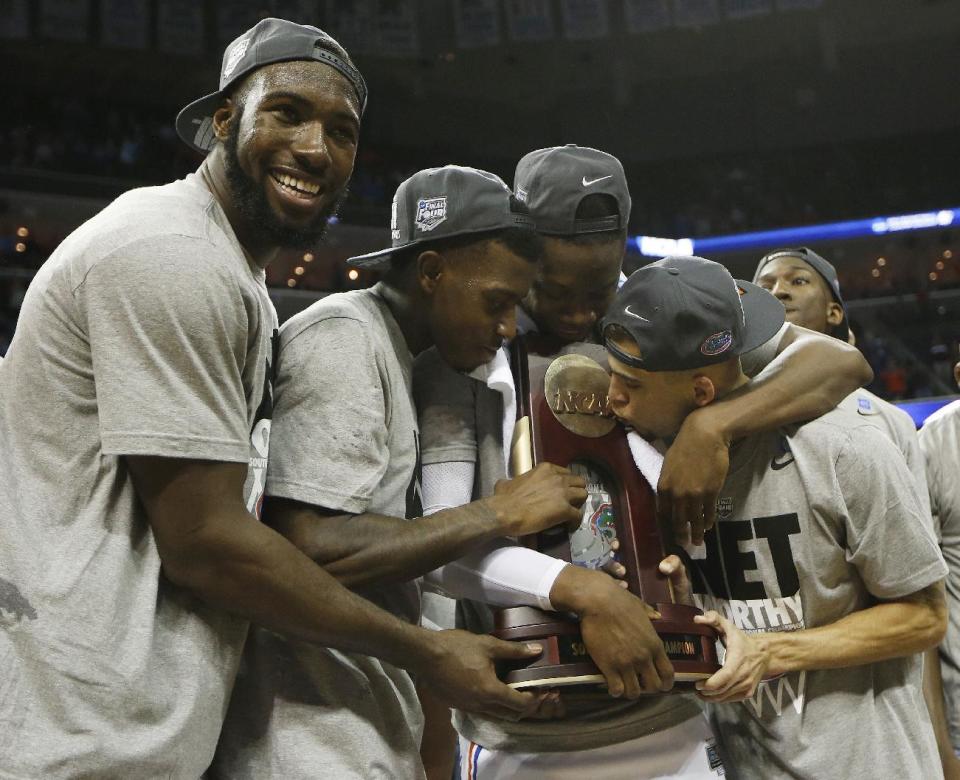 Florida guard Scottie Wilbekin, right, kisses the NCAA trophy standing with team mates after the second half in a regional final game against Dayton at the NCAA college basketball tournament, Saturday, March 29, 2014, in Memphis, Tenn. Florida won 62-52. (AP Photo/Mark Humphrey)